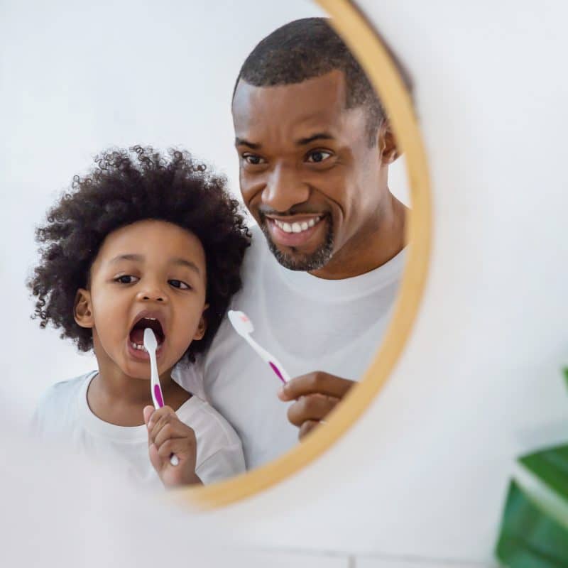 Father and child brushing teeth in mirror