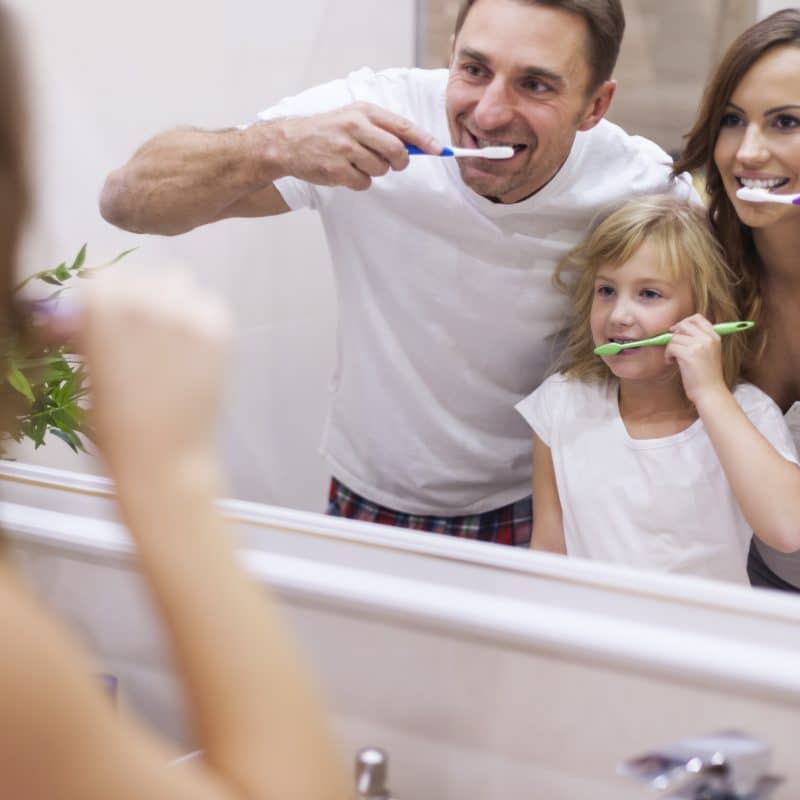 Family brushing teeth together in bathroom mirror