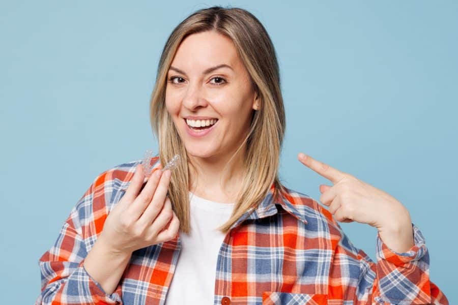 Woman smiling, holding invisible aligners, blue background