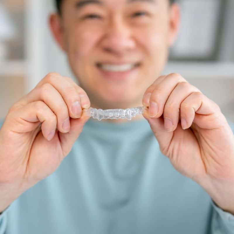 Man smiling, holding clear dental aligner in Reno & Sparks, Nevada