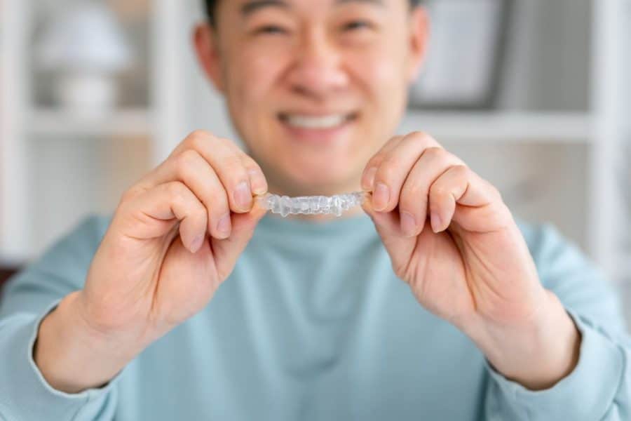 Man smiling, holding clear dental aligner in Reno & Sparks, Nevada
