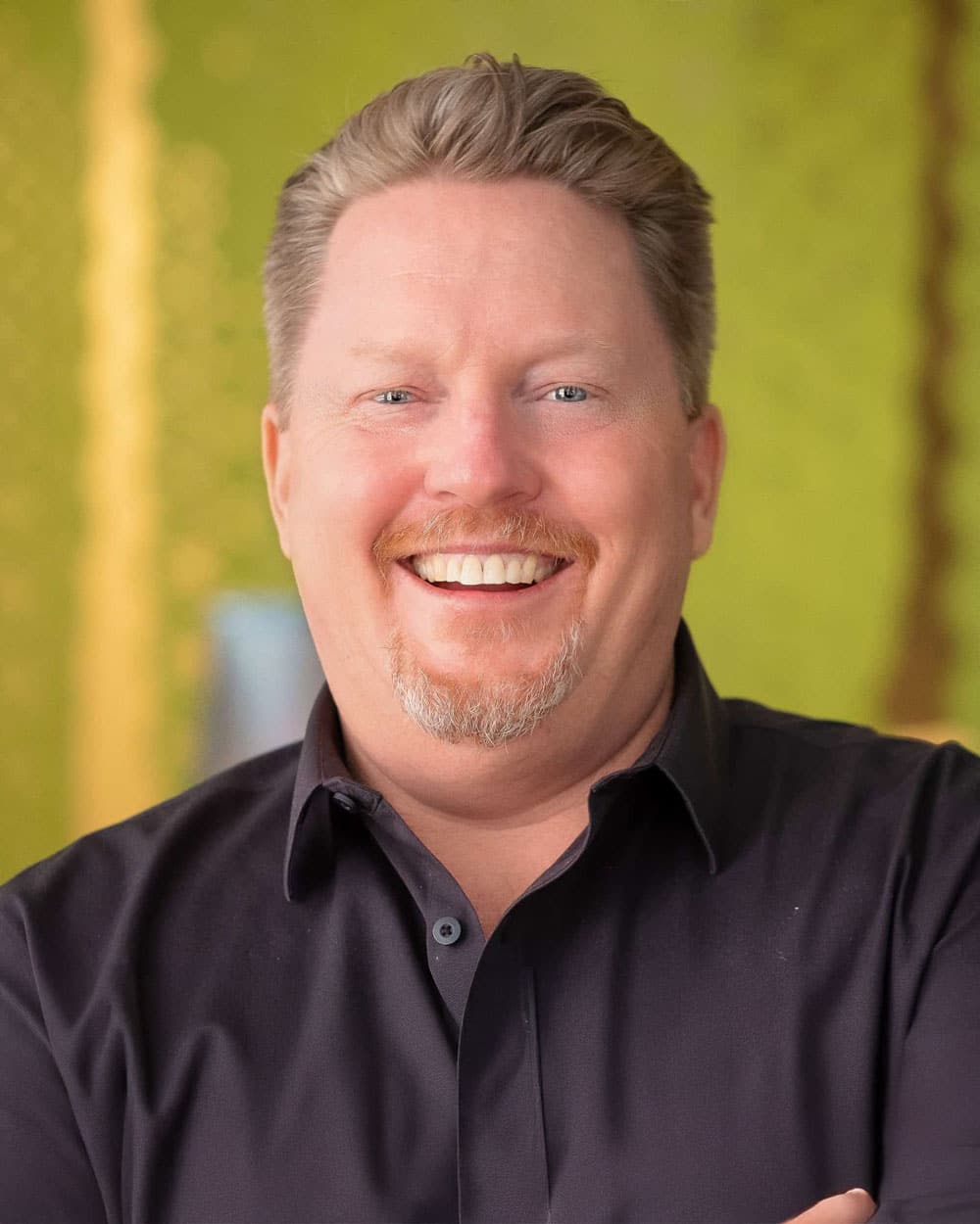 Smiling man with black shirt in front of green background