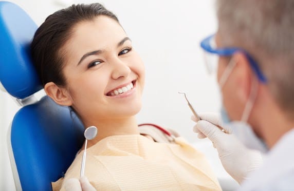 Dentist performing checkup on smiling female patient